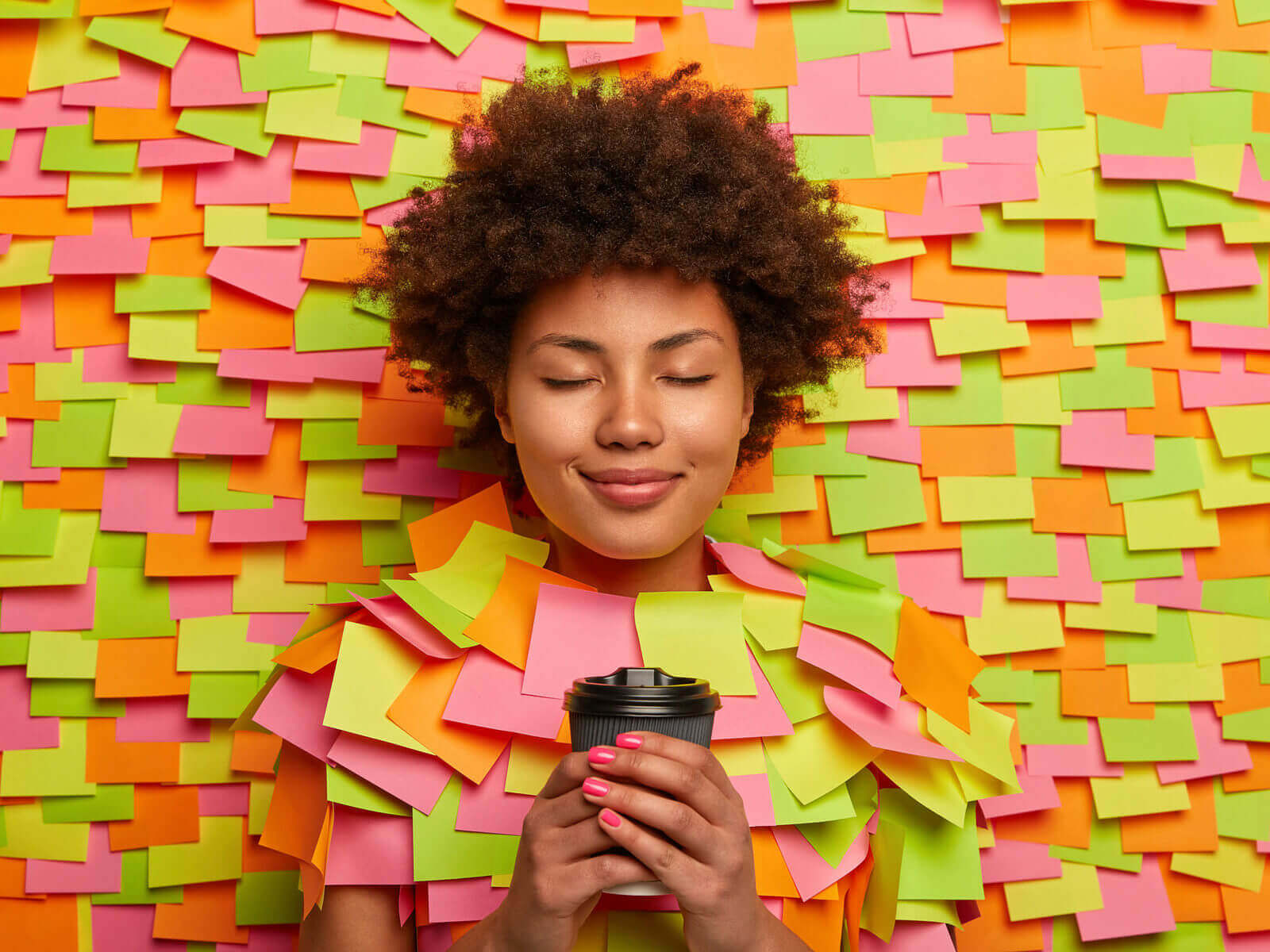 Calm relaxed woman drinks coffee on bed of post it notes.